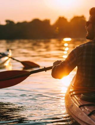 Dos personas en kayak remando al atardecer en un lago de un parque vacacional con alojamiento glamping.