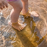 Pies descalzos de un niño jugando en agua poco profunda junto a la arena en un parque con glamping.