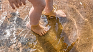 Blote kinder voeten spelen in het ondiepe water bij zand in een vakantiepark met glamping.