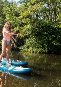 Mujer haciendo paddle surf en un río tranquilo cerca de un parque vacacional con alojamientos glamping.