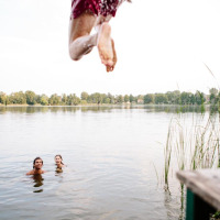 Dos personas nadan en un lago cerca de Senonches, Francia, mientras otra salta al agua desde una plataforma.