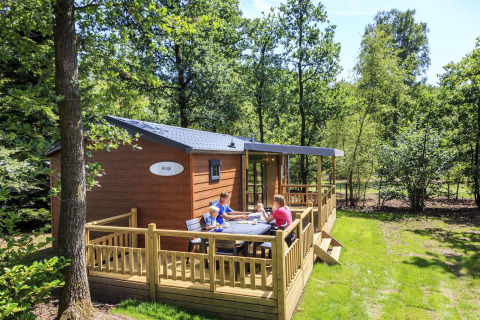 Familie nyder en solrig dag på terrassen ved en hytte i Veluwecamping De Pampel i Holland.