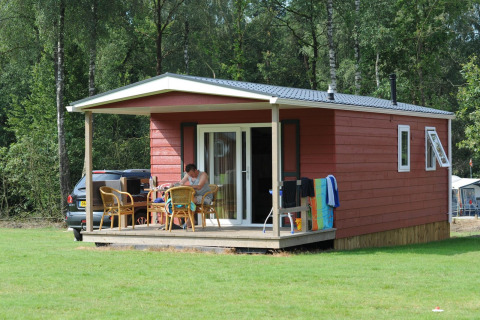 Cabaña roja en Veluwecamping De Pampel en Países Bajos, con terraza y muebles de jardín en el bosque.