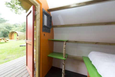 Interior de una cabaña en Veluwecamping De Pampel, con estantes verdes y puerta abierta hacia el césped.