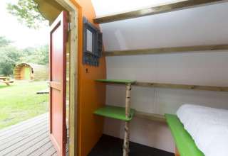 Interno di una baita a Veluwecamping De Pampel con mensole verdi, palo in betulla e porta aperta sul prato.