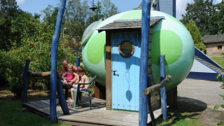 Familia sentada fuera del pod Soñando en un huevo de dragón en Veluwecamping 't Schinkel, Países Bajos.