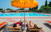 Dos personas descansan bajo una sombrilla amarilla junto a la piscina en SunLodge Katsura, Camping Gasparina, Italia.