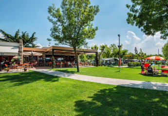 Area esterna di SunLodge Katsura al Camping Gasparina in Italia con prato verde e tavolini all’aperto.
