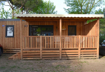 Photo of SunLodge Babul, a wooden lodge with covered porch, nestled among green trees and nature.