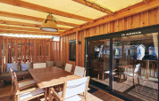 Terraza cubierta de lodge con mesa de comedor de madera, sillas, cojines y puerta corredera de cristal.