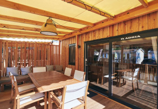 Terraza cubierta de lodge con mesa de comedor de madera, sillas, cojines y puerta corredera de cristal.