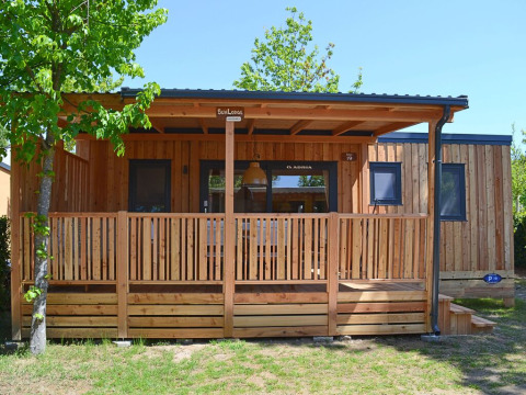 Modern wooden lodge SunLodge Sabai at Camping Gasparina in Italy, featuring a covered veranda and natural setting.
