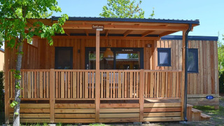 SunLodge Sabai, un pavillon en bois moderne avec terrasse couverte au Camping Gasparina en Italie, entouré de verdure.