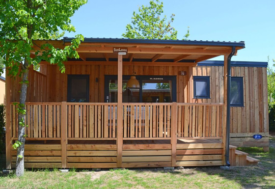 Moderne træhytte, SunLodge Sabai, ved Camping Gasparina i Italien med overdækket terrasse og grønne omgivelser.