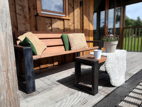 Banco de madera con cojines y mesa en la terraza de Ackerlodge, Ackerlodges Ruinerwold BV, Países Bajos.