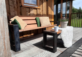 Banco de madera con cojines y mesa en la terraza de Ackerlodge, Ackerlodges Ruinerwold BV, Países Bajos.