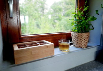 Reborde de ventana en Ackerlodge, Ruinerwold BV, con taza de té, caja de madera y planta en maceta.