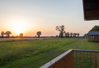 Coucher de soleil sur des champs verts et des arbres, vu d'une terrasse en bois à Ackerlodges Ruinerwold, Drenthe.