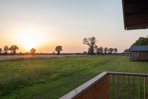 Coucher de soleil sur des champs verts et des arbres, vu d'une terrasse en bois à Ackerlodges Ruinerwold, Drenthe.