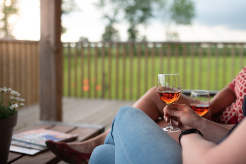 To personer nyder et glas rosévin på verandaen ved Ackerlodge, med grøn udsigt i Ruinerwold, Holland.