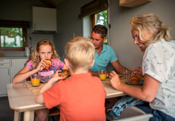 Gezin geniet van ontbijt met croissants en sinaasappelsap in Ackerlodge, Ackerlodges Ruinerwold BV, Nederland.