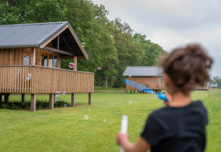 Child playing with bubbles in front of wooden cabins at Ackerlodges Ruinerwold holiday park, Drenthe, Netherlands.
