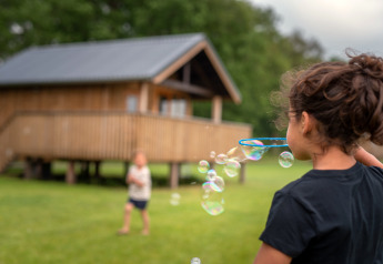 Kinderen spelen met zeepbellen voor een houten lodge bij Ackerlodge, Ackerlodges Ruinerwold BV, Nederland.