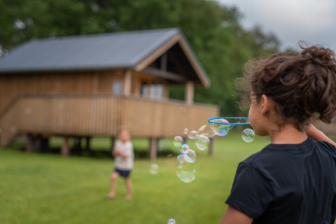 Kinderen blazen bellen voor een houten lodge bij Ackerlodge, Ackerlodges Ruinerwold BV in Nederland.
