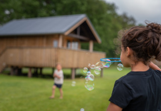 Kinderen blazen bellen voor een houten lodge bij Ackerlodge, Ackerlodges Ruinerwold BV in Nederland.