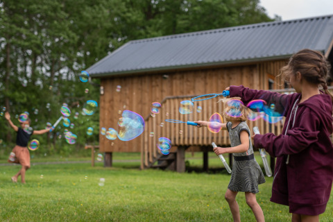 Kinderen spelen met zeepbellen voor een houten lodge in Ackerlodges Ruinerwold BV vakantiepark in Drenthe, Nederland.