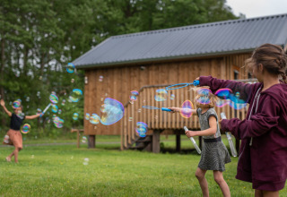 Kinder spielen mit Seifenblasen vor einer Holzhütte im Ackerlodges Ruinerwold BV Ferienpark in Drenthe, Niederlande.