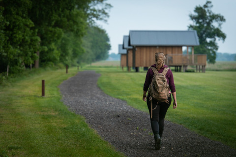 Femme avec sac à dos marchant sur un sentier vers des cabanes modernes à Ackerlodges Ruinerwold, Drenthe, Pays-Bas.