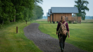 Mujer con mochila camina por un sendero hacia cabañas modernas en Ackerlodges Ruinerwold, Drenthe, Países Bajos.
