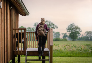 Frau mit Rucksack steigt eine Treppe zur Holzhütte im Ackerlodges Ruinerwold BV, Drenthe, Niederlande hinauf.