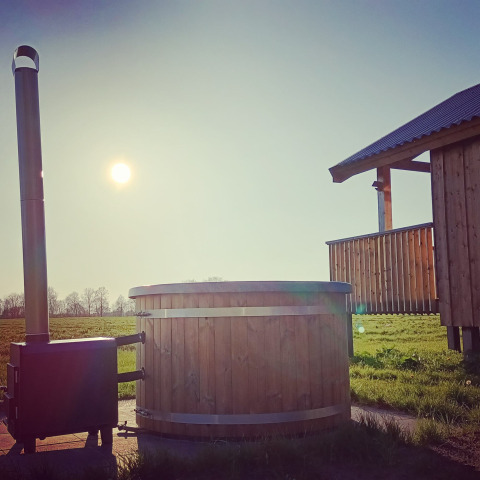 Luz del sol sobre una cabaña y bañera de madera en Ackerlodges Ruinerwold BV, parque vacacional en Drenthe, Países Bajos.