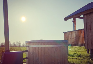 Sollys over en træhytte og udendørs vildmarksbad ved Ackerlodges Ruinerwold BV feriepark i Drenthe, Holland.
