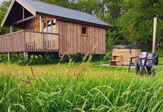 Wooden cabin with a porch and outdoor hot tub in lush greenery at Ackerlodges Ruinerwold, Drenthe.