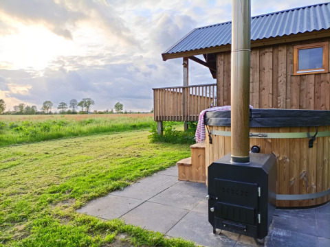 Outdoor scene with wooden cabin, hot tub, and fields at Ackerlodges Ruinerwold BV holiday park in Drenthe, Netherlands.