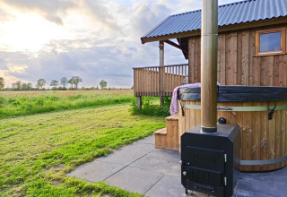 Buitenzicht met houten chalet, hottub en weiland bij Ackerlodges Ruinerwold BV in Drenthe, Nederland.