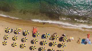 Vista aérea de una playa con sombrillas azules y amarillas y agua clara en un parque de vacaciones.