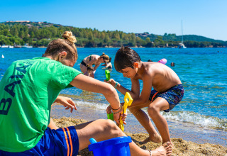 Dos niños juegan en la arena junto al agua en un parque vacacional con glamping, rodeados de naturaleza.