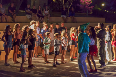 Niños y adolescentes participan en animación nocturna con animadores disfrazados en un camping glamping.