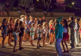 Kinderen en jongeren nemen deel aan avondanimatie met verklede entertainers op een glamping vakantiepark.