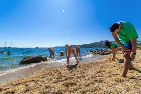 Holiday park guests enjoying fitness or stretching exercises on a sandy beach by the ocean under blue skies.