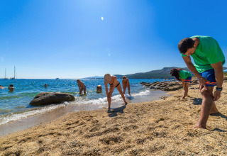 Holiday park guests enjoying fitness or stretching exercises on a sandy beach by the ocean under blue skies.