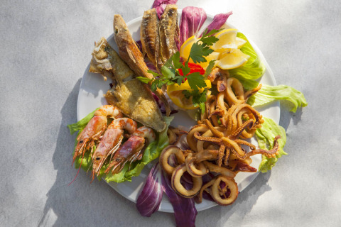 Un plato de mariscos variados con gambas, calamares fritos y pescado, servido con lechuga y limón.