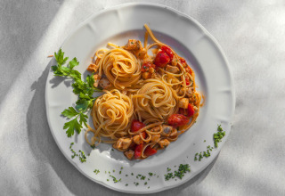 Piatto di spaghetti con pomodorini, bocconcini di pollo e prezzemolo, servito su un piatto bianco.