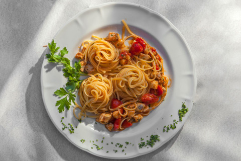 En appetitlig tallerken med spaghetti, tomater, kyllingebidder og persille serveret på en hvid tallerken.