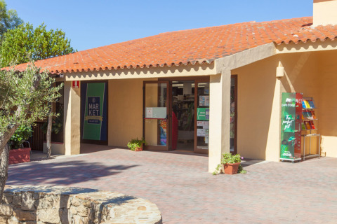 Entrada a un mercado en un parque vacacional en un día soleado con techo de tejas, ambiente glamping.