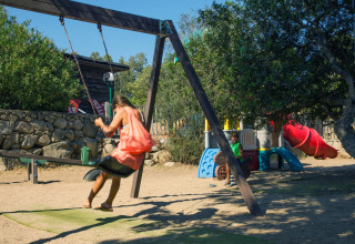 Bambini che giocano su un parco giochi con altalena e scivolo in un villaggio vacanze glamping al sole.